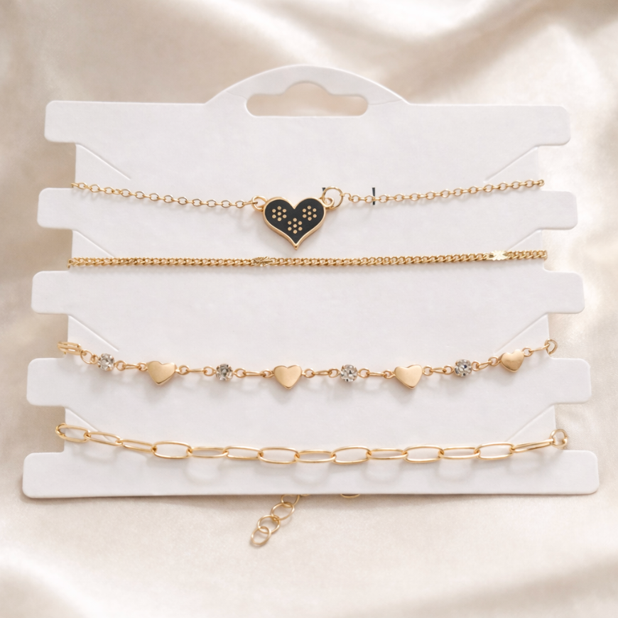 Set of gold bracelets with heart and chain designs on a white card.