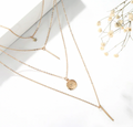 Flat-lay product shot of Violet Vows gold multi-layered necklace with star, bar, and coin charms