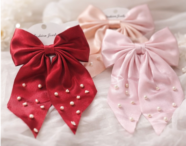 Red and pink pearl bow hair clips with long satin ribbon tails on white fabric background