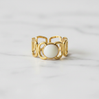 Gold geometric cutout wide band ring with white oval stone on white marble surface