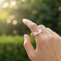 Gold white enamel angel wings open cuff ring worn on finger with soft garden bokeh