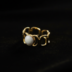 Gold geometric cutout wide band ring with white oval stone on black velvet with dramatic rim lighting