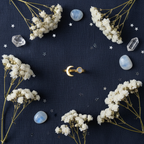 Gold moon and moonstone ring flat lay with crystals and star confetti on navy linen