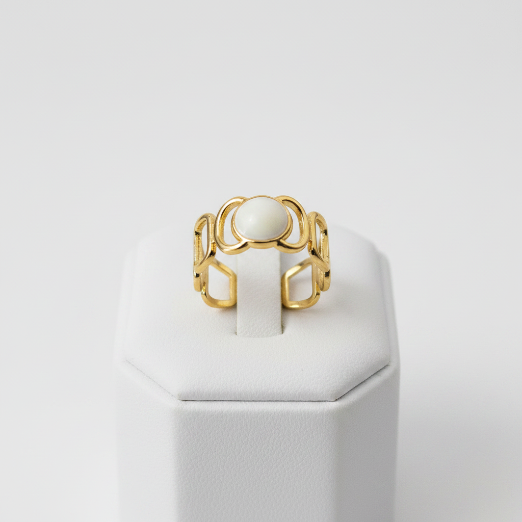 Gold geometric cutout wide band ring with white oval stone on white jewelry stand, clean studio shot