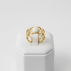 Gold geometric cutout wide band ring with white oval stone on white jewelry stand, clean studio shot