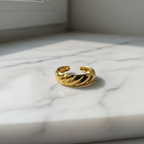Gold twisted croissant open band ring on white marble surface