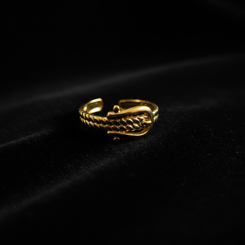 Gold belt buckle braided chain open cuff ring on black velvet with dramatic rim lighting
