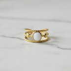 Gold triple twisted rope band white oval stone open cuff ring on white marble surface
