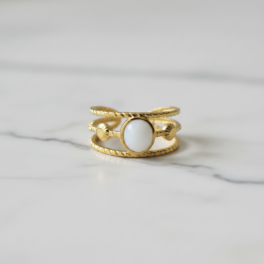 Gold triple twisted rope band white oval stone open cuff ring on white marble surface