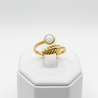 Gold leaf and white stone bypass open cuff ring on white jewelry stand, clean studio shot