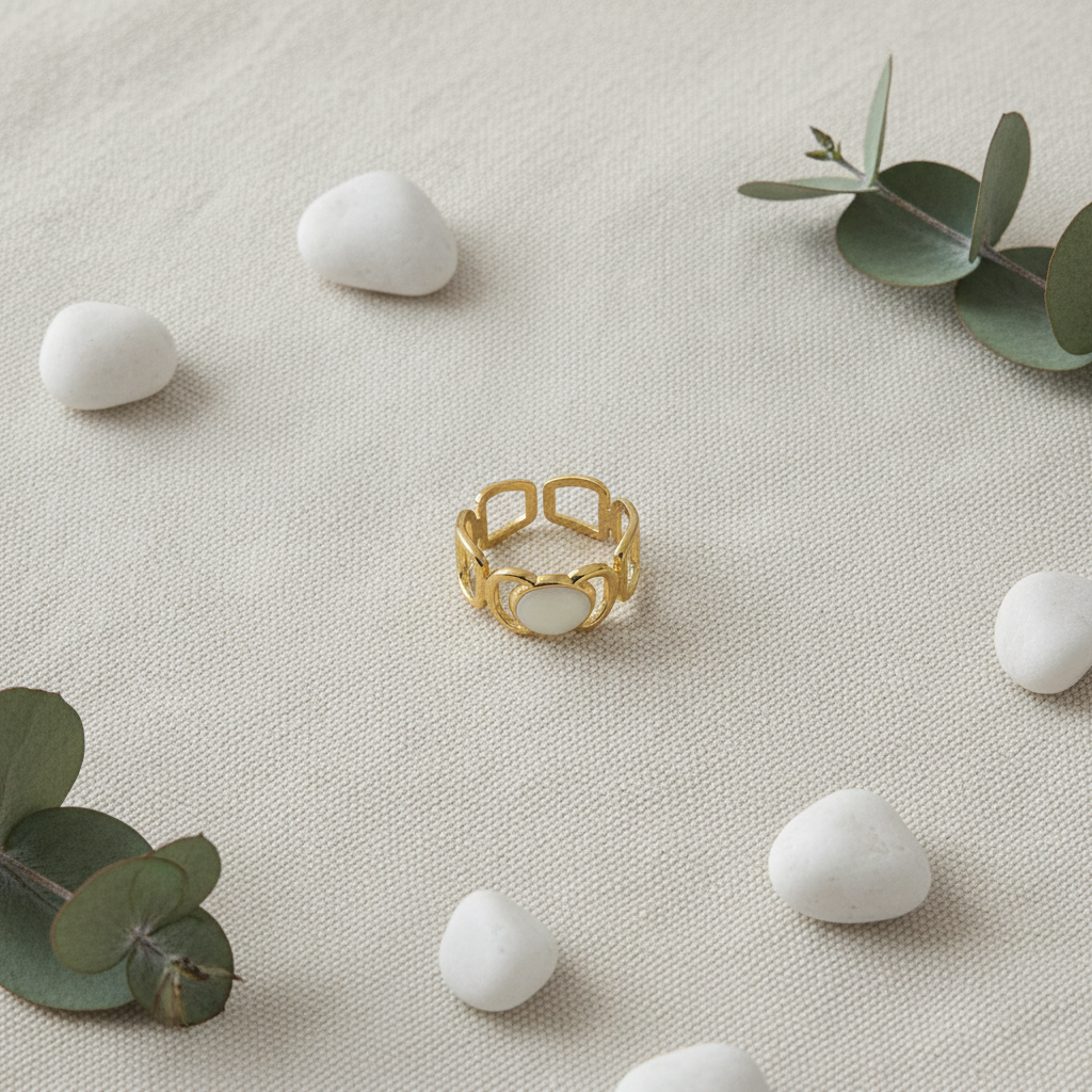 Gold geometric cutout wide band ring with white oval stone on ivory linen with white pebbles and eucalyptus