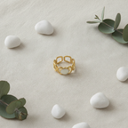 Gold geometric cutout wide band ring with white oval stone on ivory linen with white pebbles and eucalyptus