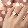 Gold chain link band white enamel heart open cuff ring worn on finger with romantic pink and golden bokeh