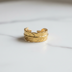 Gold feather engraved open cuff ring on white marble surface