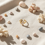 Gold white enamel starfish open cuff ring on sandy beige linen with seashells and dried coral