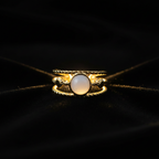 Gold triple twisted rope band white oval stone open cuff ring on black velvet with dramatic rim lighting