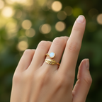 Gold leaf and white stone bypass open cuff ring worn on finger with lush botanical bokeh