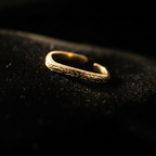Gold engraved floral band open cuff ring on black velvet with dramatic rim lighting