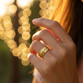 Gold feather engraved open cuff ring worn on finger with warm golden bokeh