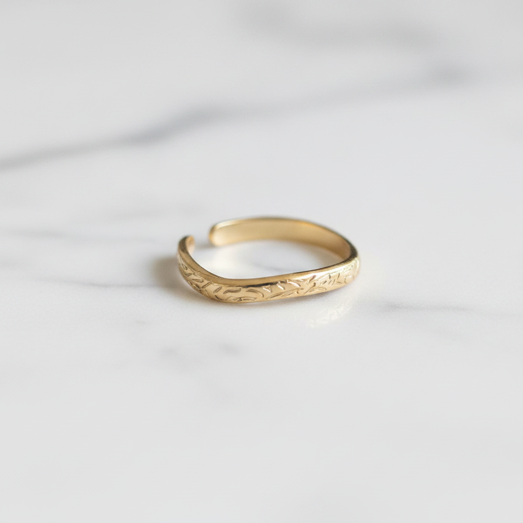 Gold engraved floral band open cuff ring on white marble surface