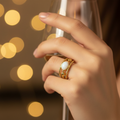 Gold triple twisted rope band white oval stone open cuff ring worn on finger with warm golden bokeh