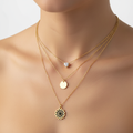 Model wearing Violet Vows gold triple-layer necklace featuring a heart crystal, disc, and sunflower pendant.