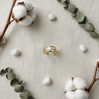 Gold triple twisted rope band white oval stone open cuff ring on ivory linen with white pebbles and eucalyptus