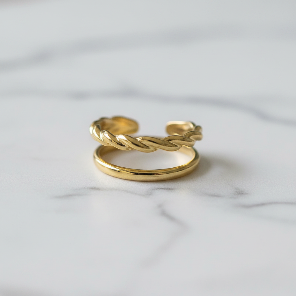 Gold double band twisted rope and plain open cuff ring on white marble surface
