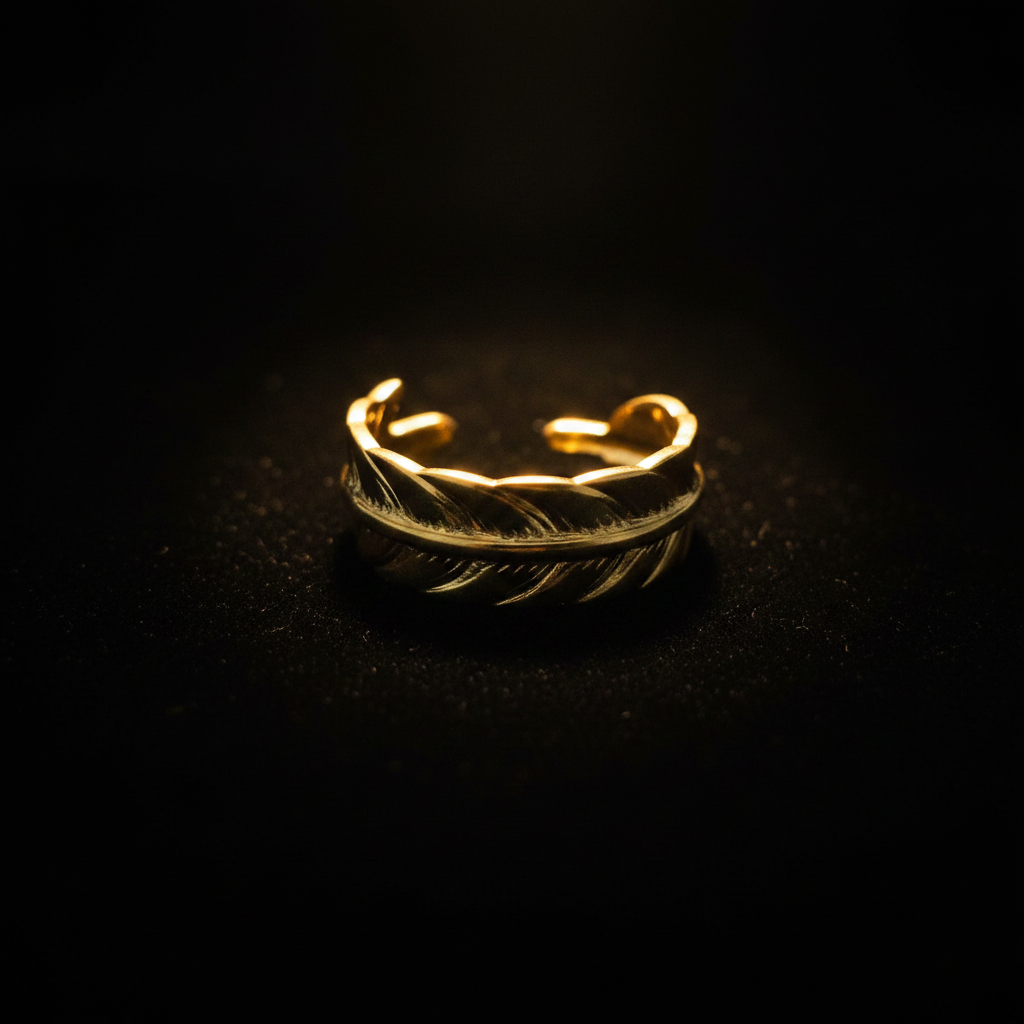 Gold feather engraved open cuff ring on black velvet with dramatic rim lighting