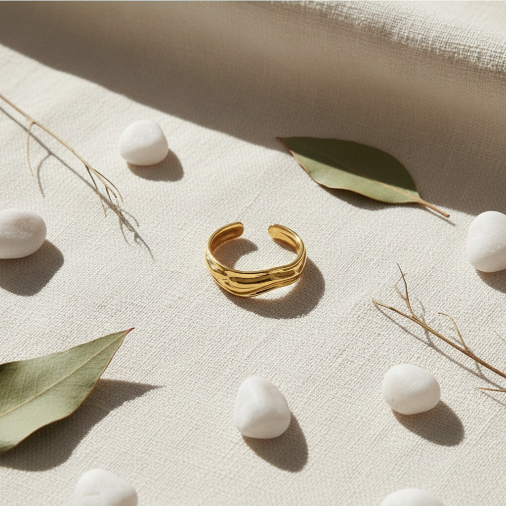 Gold molten wave sculptural open cuff ring on ivory linen with white pebbles and eucalyptus