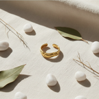 Gold molten wave sculptural open cuff ring on ivory linen with white pebbles and eucalyptus